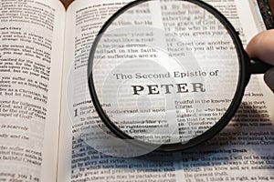closeup of The second epistle of Peter from Bible using a magnifying glass to enlarge print.
