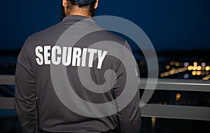 Closeup of a security guy in a dark gray uniform standing near a handrail.