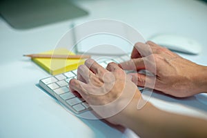 Closeup selective focus on hands of businessman typing on the keyboard with defocused stationaries in background