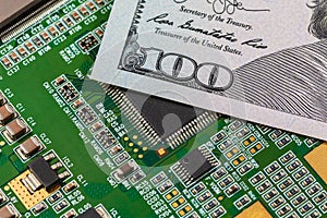 Closeup of semiconductor circuit board and 100 dollar bill