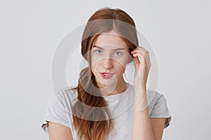 Closeup of sensual beautiful young woman with red hair and freckles standing and looking directly in camera isolated over white