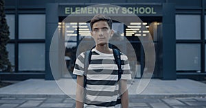 Closeup serious teen boy standing at schoolyard. Tensed schoolboy posing alone.