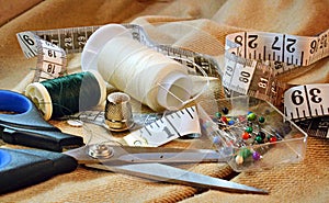 Closeup of sewing kit on fabric background including scissors, thread bobbins, measuring tape, thimble and pins