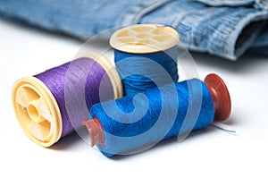 Sewing thread spool bobbin on white table on blue jeans background