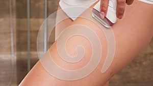 Closeup of sexy woman using epilator to remove hair from skin on legs in bathroom. Concept of female beauty, body care