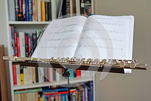 Closeup of a shiny flute against a musical score with a bookshelf in the background