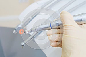 Closeup shoot of doctor hand holding dental instruments in clinic, turbines, handpieces and drills at background.