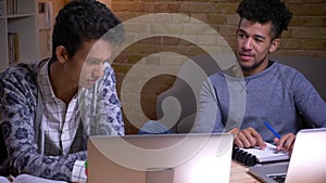 Closeup shoot of indian and african american male students using the laptops and discussing a college project sitting