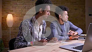 Closeup shoot of indian and african american male students using the laptops and discussing a project laughing