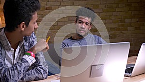 Closeup shoot of indian and african american male students using the laptops having a discussion and gesturing sitting