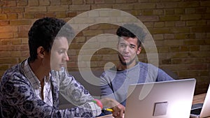 Closeup shoot of indian and african american male students using the laptops having a discussion indoors in the library