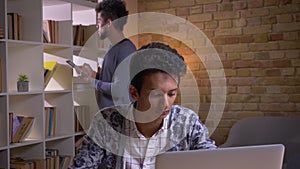 Closeup shoot of two culturally diverse students learning in the college library indoors. Indian male studying online on