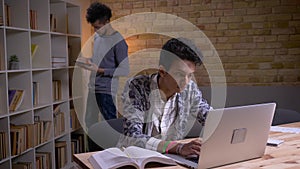 Closeup shoot of two culturally diverse students learning in the library indoors. Indian male studying online on the
