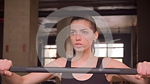 Closeup shoot of young attractive athlete female walking and getting ready to lift weights with determination in the gym