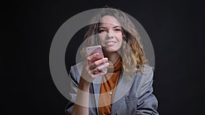 Closeup shoot of young attractive caucasian female messaging on the phone and smiling while looking at camera