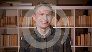 Closeup shoot of young attractive caucasian male student smiling and waving hi looking at camera in the college library