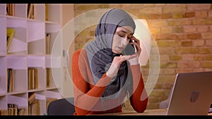 Closeup shoot of young attractive muslim female employee in hijab having a conversation on the phone while typing on the