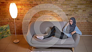 Closeup shoot of young attractive muslim female having a phone call resting laidback on the couch indoors at cozy home