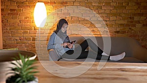 Closeup shoot of young attractive muslim female surfing web on the phone while resting laidback indoors at cozy home