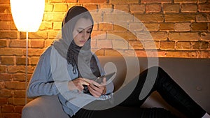 Closeup shoot of young attractive muslim female using social media on the phone while resting laidback indoors at cozy