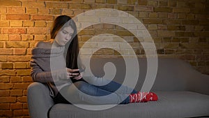 Closeup shoot of young cute caucasian female messaging on the phone while resting laidback on the sofa at cozy home