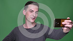 Closeup shoot of young handsome caucasian male having a video call on the phone with background isolated on green