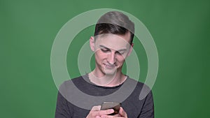 Closeup shoot of young handsome caucasian male messaging on the phone with background isolated on green