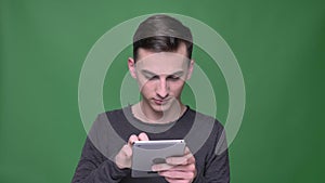 Closeup shoot of young handsome caucasian male messaging on the tablet with background isolated on green