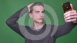 Closeup shoot of young handsome caucasian male taking selfies on the phone with background isolated on green