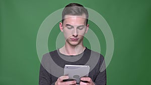 Closeup shoot of young handsome caucasian male using the tablet with background isolated on green