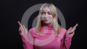 Closeup shoot of young pretty blonde female having her fingers crossed and being anxious and worried looking at camera