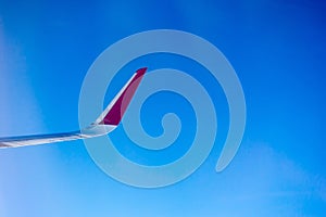 Closeup shot of an airplane wing in red and white colors isolated on the blue sky