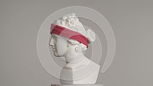 Closeup shot. Ancient marble bust statue of roman era woman in sport headband spinning on a platform. Isolated on grey