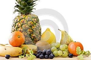 Closeup shot of assorted different fruits on a wooden table with a white background behind