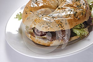 Closeup shot of a bagel of ham and lettuce on white plate