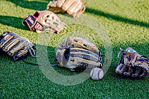 Closeup shot of baseball gloves and a ball on green grass