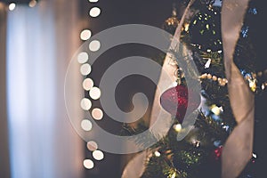 Closeup shot of a beautiful red ornament on the Christmas tree with bokeh lights in the background