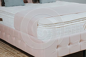 Closeup shot of a bed with pink fabric upholstery, white mattress, blanket and cushions