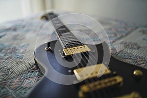 Closeup shot of a black electric guitar on a bed with patterned sheet