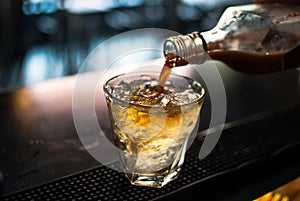 Closeup shot of blended whiskey being poured in a glass from a bottle with blurred background