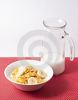 Closeup shot of a bowl of cornflakes and banana and a pitcher of milk