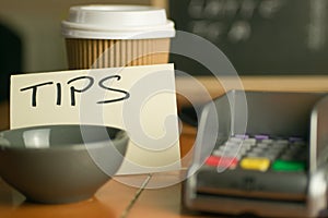 Closeup shot of a bowl near a contactless pdq machine and a tips note leaning on a coffee cup