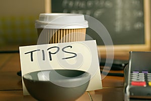 Closeup shot of a bowl near a contactless pdq machine and a tips note leaning on a coffee cup