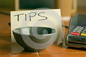 Closeup shot of a bowl near a contactless pdq machine and a tips note leaning on a coffee cup photo