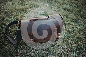 Closeup shot of a brown leather satchel on the green grass