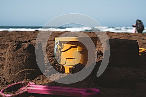 Closeup shot of a bucket in the middle of sandcastles with beach waves in the background