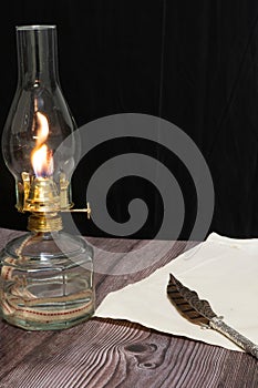 Closeup shot of a burning old antique hurricane oil lamp with quill pen and paper on wooden table