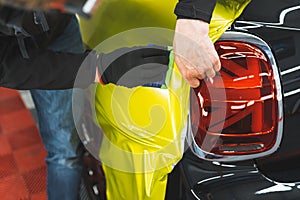 Closeup shot of car wrapping process. Two hands applying neon yellow vehicle vinyl wrap onto the surface of a black car.