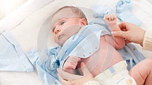 Closeup shot of caring mother undressing her little 1 months old baby boy lying on changing table. Concept of babies and