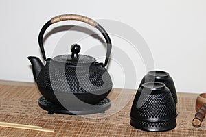 Closeup shot of a cast-iron Japanese teapot, teacups and wooden ladle